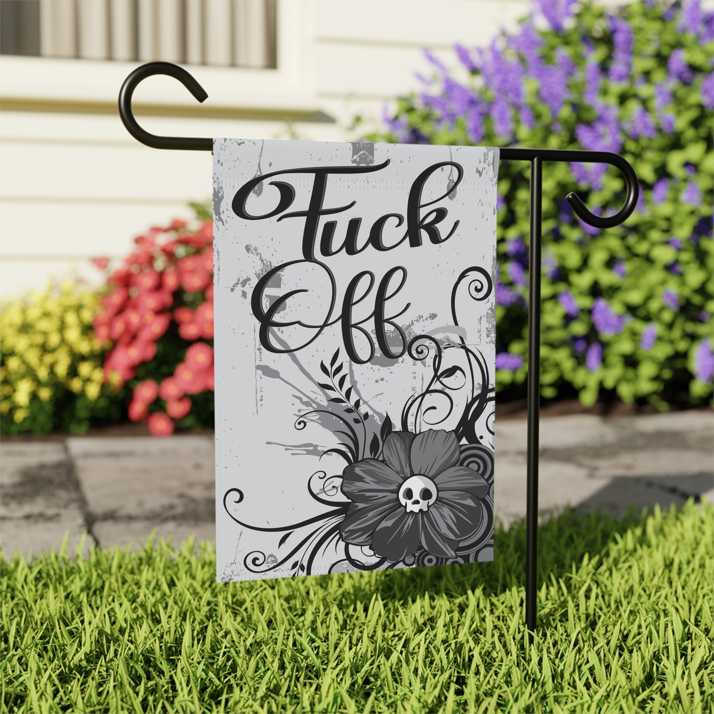 Garden flag with 'Fuck Off' in stylish script, embellished with a grey floral design and a central skull, placed in a home garden setting.