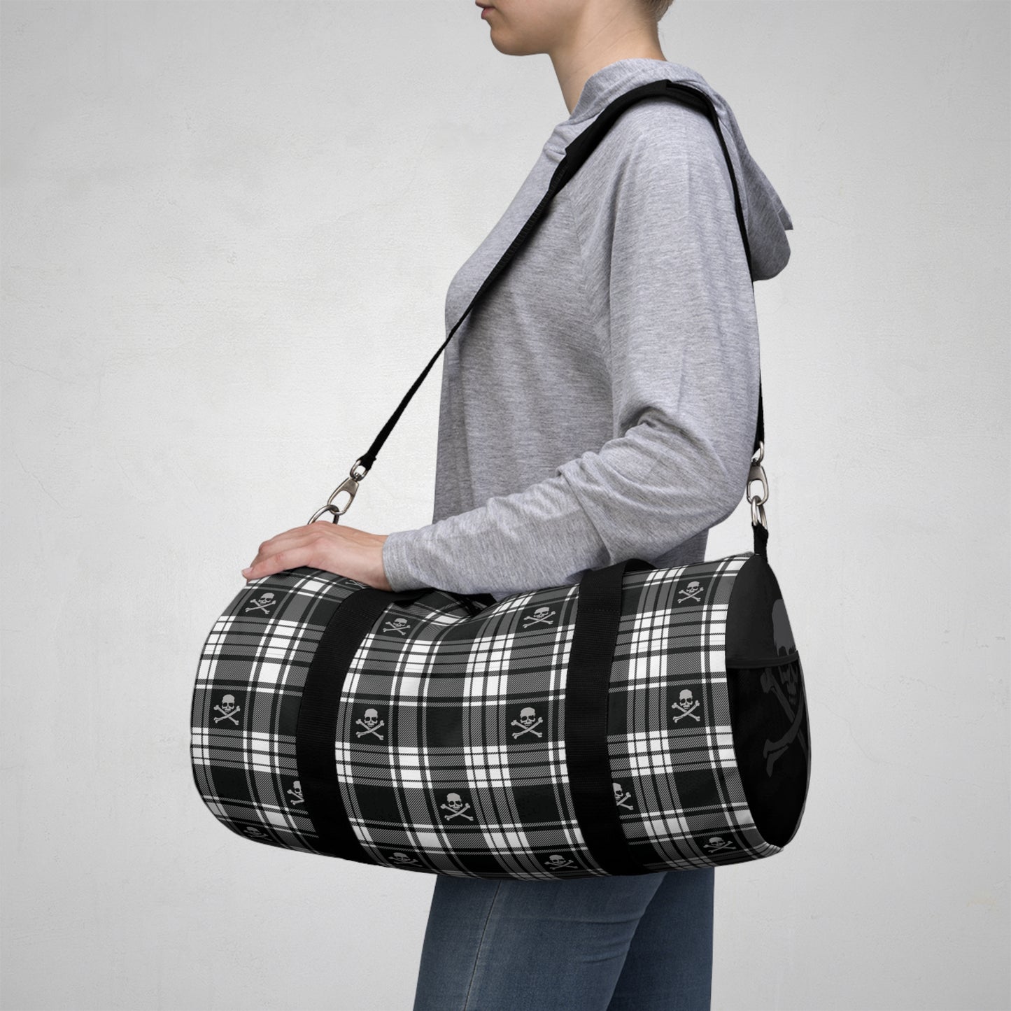Black and White Flannel Patterned Skull and Crossbones Duffel Bag side view with person holding the bag ready to board their plane flight heading on vacation